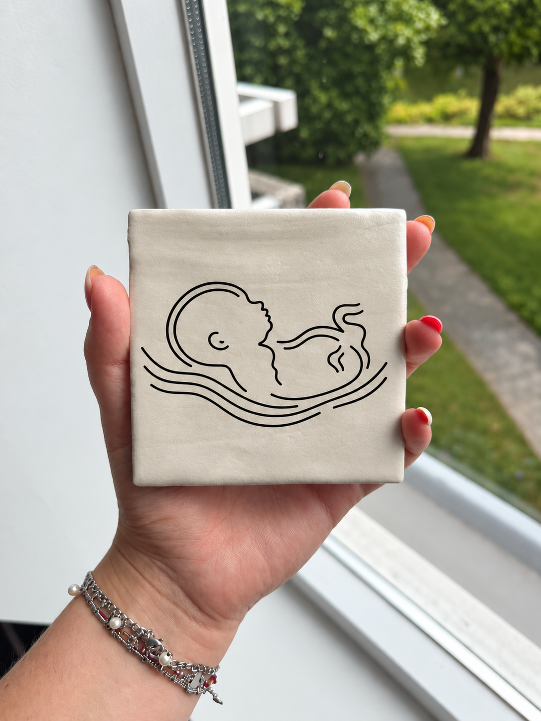 Parelmoer echo tegeltje met minimalistische baby lijntekening in de hand